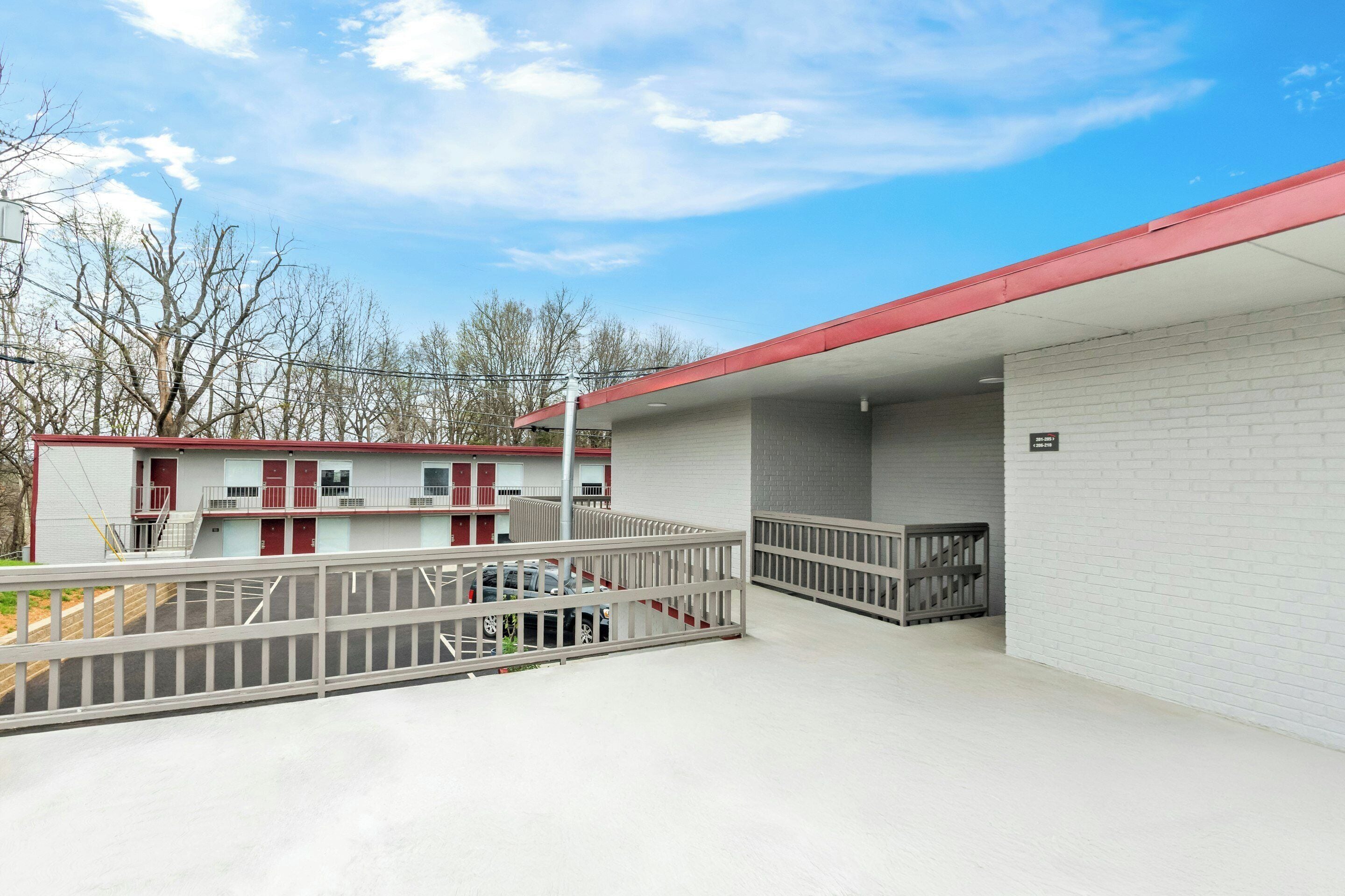 A building with a red roof, white brick walls, and a covered parking area with a white railing.