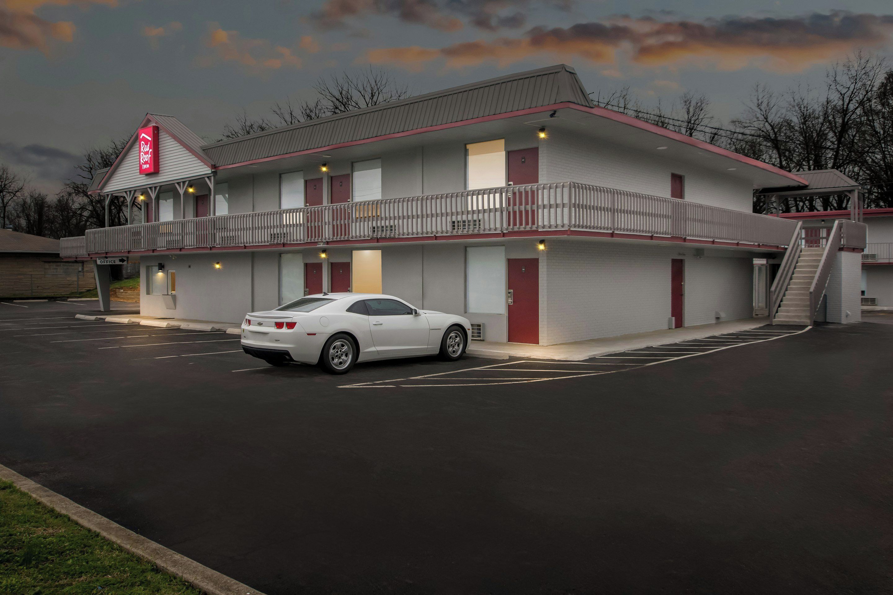 A motel with a two-story structure, a covered parking area, and a white car parked in the lot.