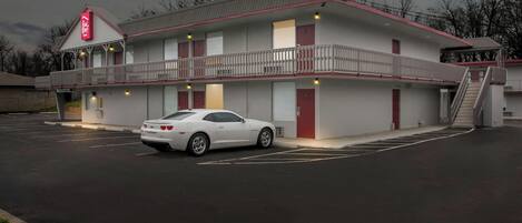 A motel with a two-story structure, a covered parking area, and a white car parked in the lot.