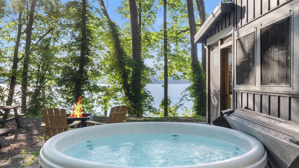 Un bain à remous avec une terrasse en bois, un foyer et une vue sur un lac.