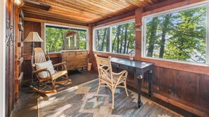 L’intérieur d’un chalet rustique, avec des murs en bois, un fauteuil à bascule, un bureau et de grandes fenêtres donnant sur la forêt.