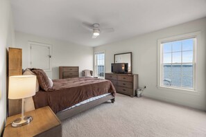 A bedroom with a bed, dresser, television, and a view of the water.