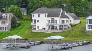 A large white house with a balcony and a dock with chairs.