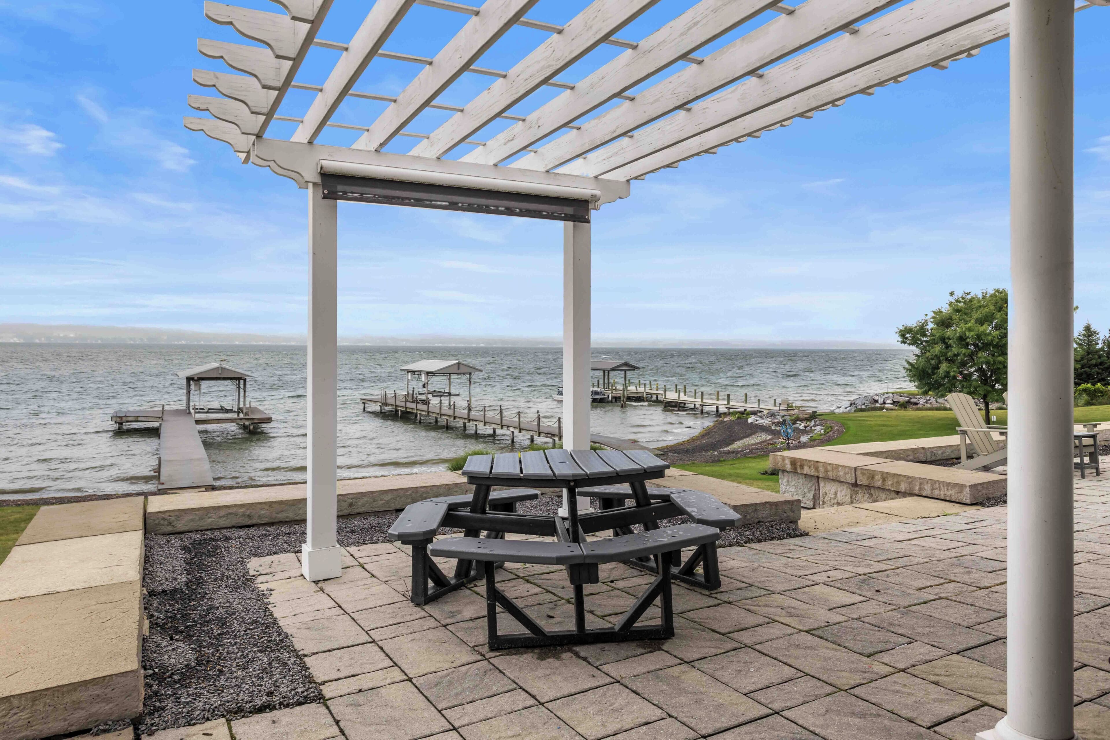 Um parque à beira-mar com um pérgola, mesas de piquenique e um cais que se estende sobre a água.
