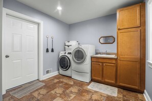 A laundry room with a washing machine, dryer, and wooden cabinets. - Gracie's Place: Stunning Lakefront Escape on Seneca Lake! (Romulus)