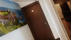 A hallway with a door, a painting on the wall, and a glimpse of a room with a bed. - Ristorante B&B Posidonia (Sapri)