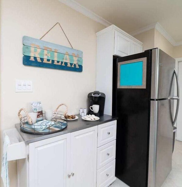 A kitchen with a black refrigerator, white cabinets, a coffee maker, and a tray with coffee cups and pastries.