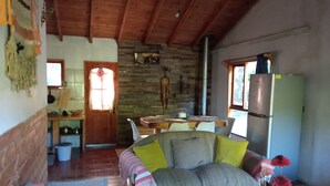 A cozy living room with a wooden ceiling, a stone fireplace, a dining table with chairs, and a refrigerator. - House with terrace near the lake, national parks and caburgua eyes (Pucon)