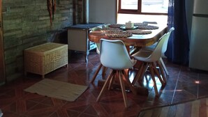 A dining area with a wooden table and chairs, a stone wall, and a window with curtains. - House with terrace near the lake, national parks and caburgua eyes (Pucon)
