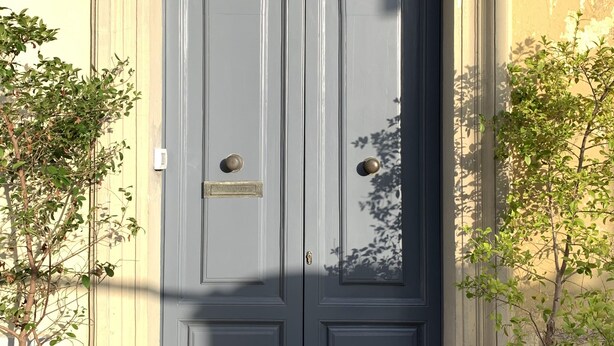 A double door with a brass handle and a nameplate, flanked by potted plants. - Palazzo Samà (Catanzaro)
