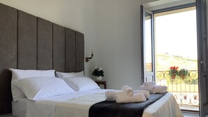 A neatly made bed with white linens, a dark headboard, and a view of the outdoors through an open door. - Palazzo Samà (Catanzaro)