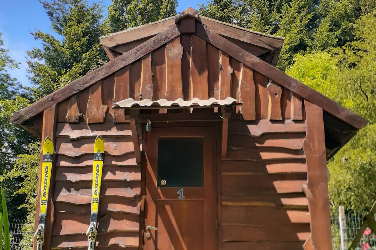 Eine kleine Holzhütte mit Tür und Fenster, umgeben von viel Grün und Bäumen.