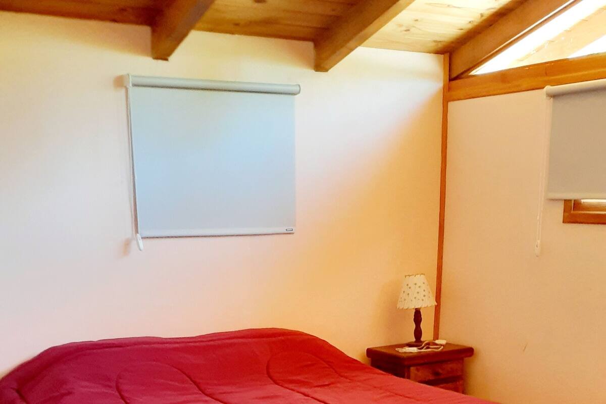 Ein Schlafzimmer mit Holzboden, einem roten Bett, einem kleinen Holztisch und einem Nachttisch mit Lampe.