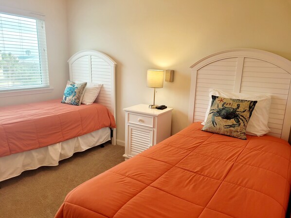 A bedroom with two beds, each with an orange bedspread and matching pillows. There is a nightstand with a lamp and a phone between the beds.