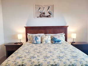 Quarto com colcha florida, duas almofadas combinando, cabeceira de madeira e uma obra de arte emoldurada de pássaros na parede.