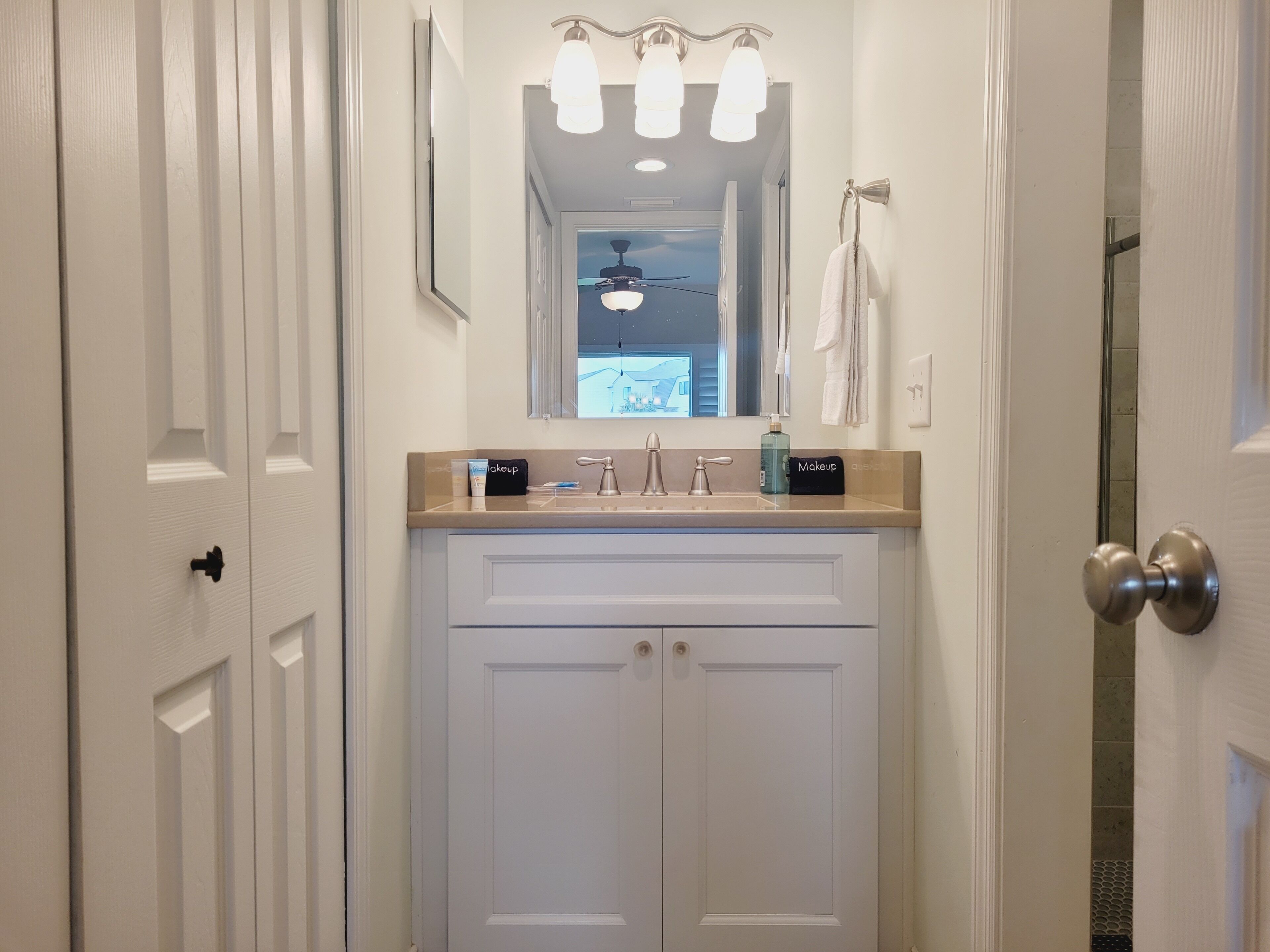 A bathroom with a double vanity, a mirror, a ceiling fan, and a towel rack.