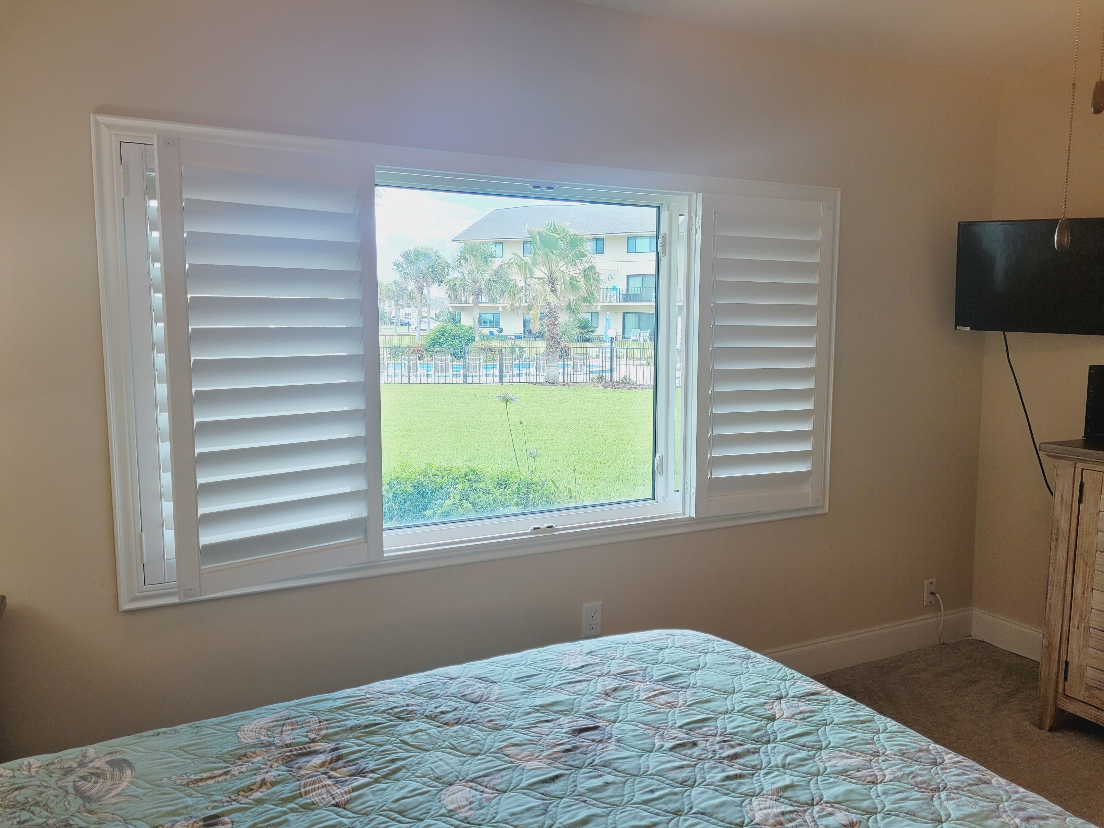 A bedroom with a bed, a TV, and a window with blinds.