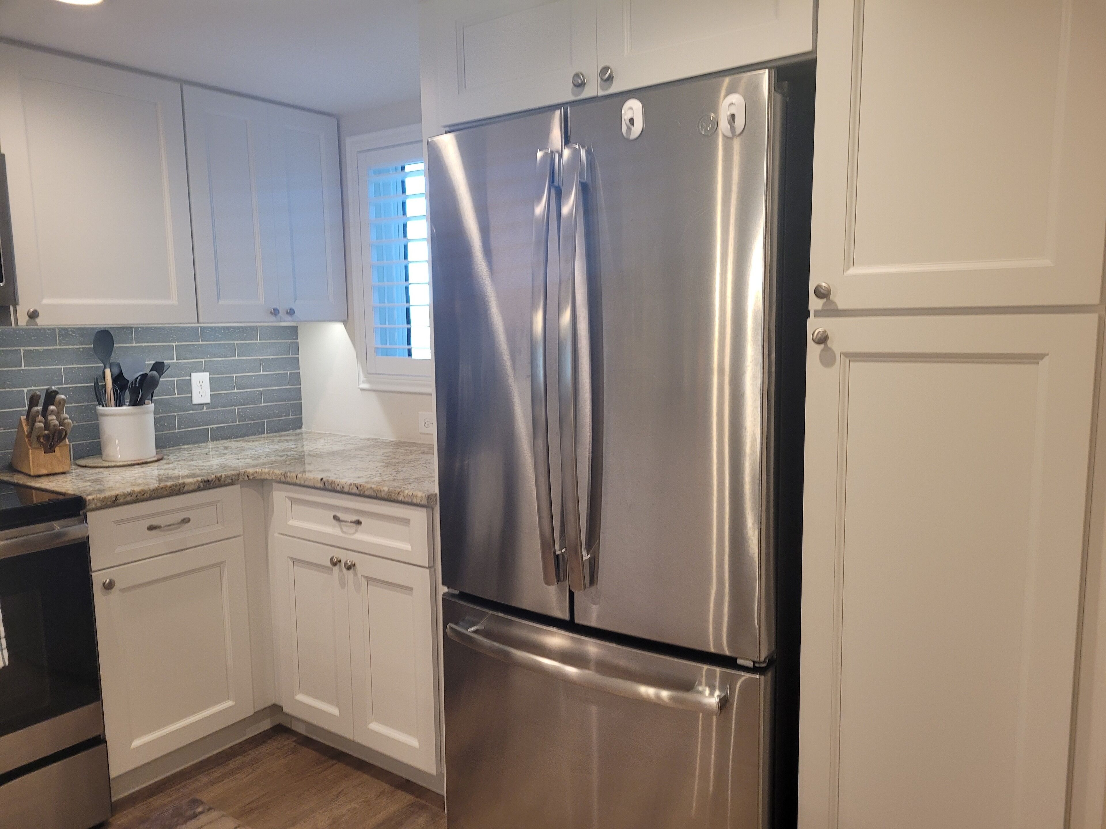 A kitchen with white cabinets, a stainless steel refrigerator, and a granite countertop.