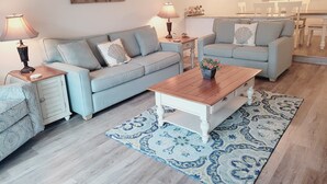 A living room with a sofa, a coffee table, a rug, and a dining area with a table and chairs. - Oceanview from balcony 3 Bedroom 2 Bath ground floor Unit - 110 (ST. AUGUSTINE)