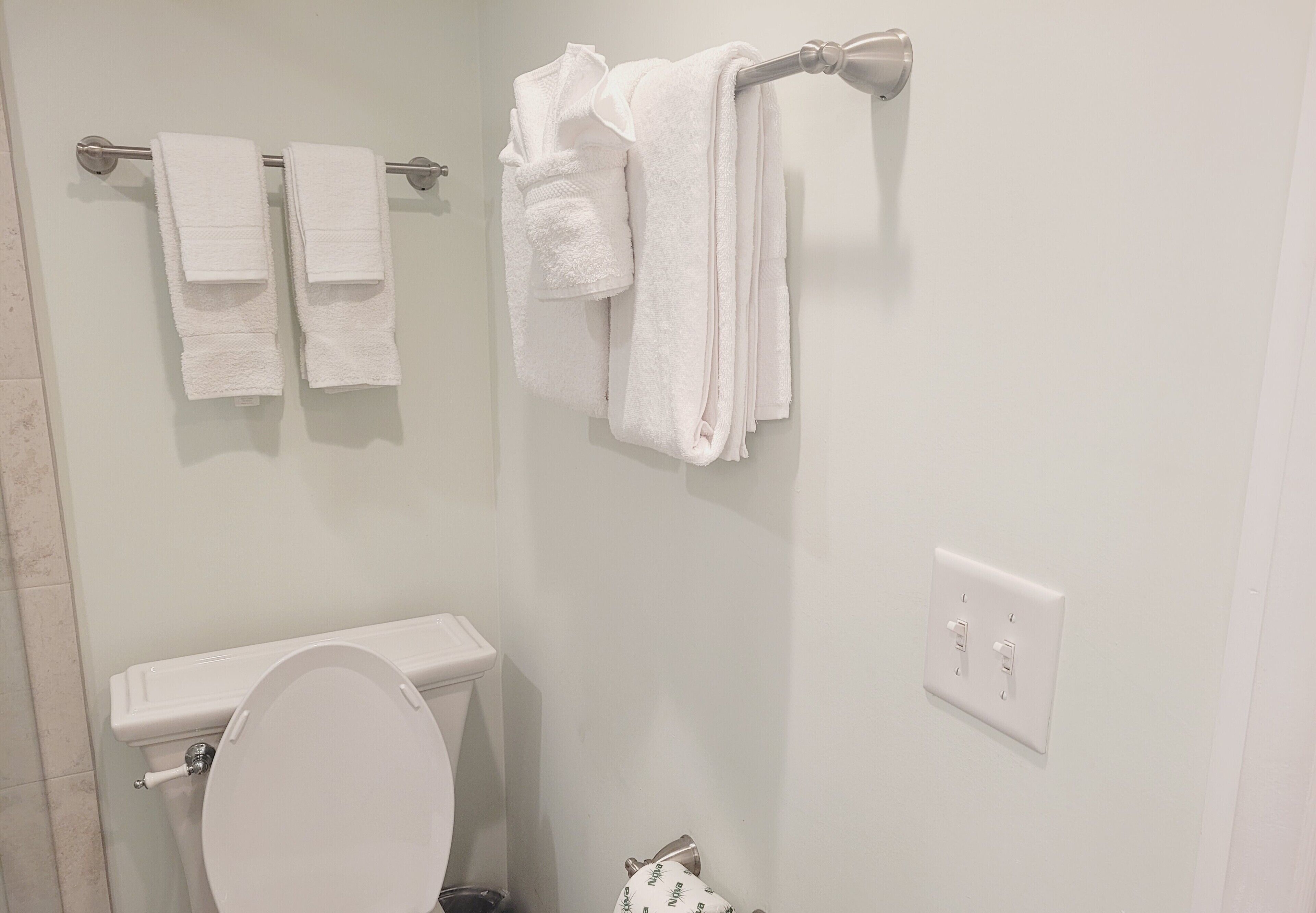 A bathroom with a toilet, two towel racks with white towels, and a light switch on the wall.