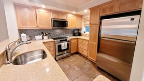Una cocina moderna con armarios de madera, electrodomésticos de acero inoxidable, microondas, cafetera y refrigerador.