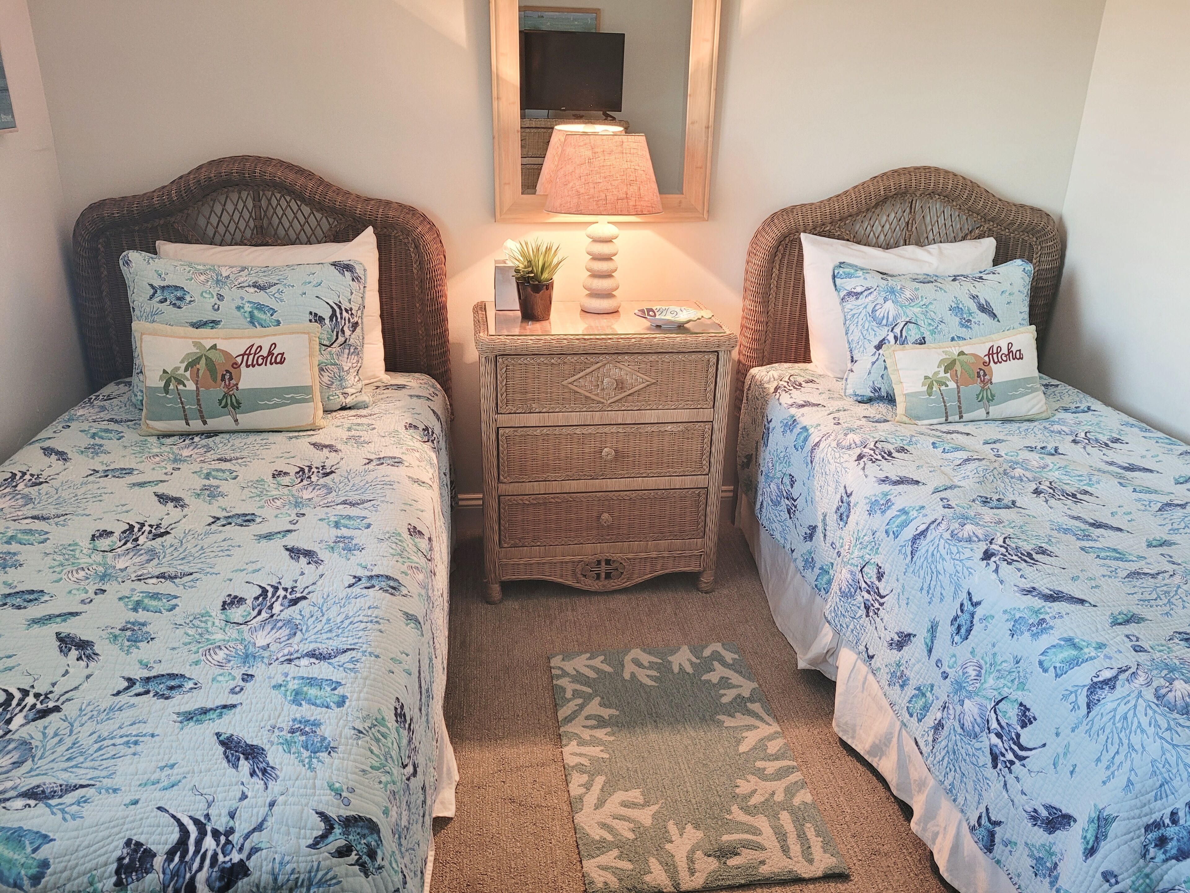 Una habitación con dos camas, cada una con cubrecama y almohadas de flores azules a juego. Hay una mesita de mimbre con una lámpara y una pequeña planta en maceta entre las camas.