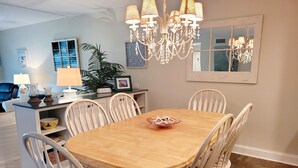 Un comedor con una mesa de madera y sillas blancas, una araña y una planta en maceta.