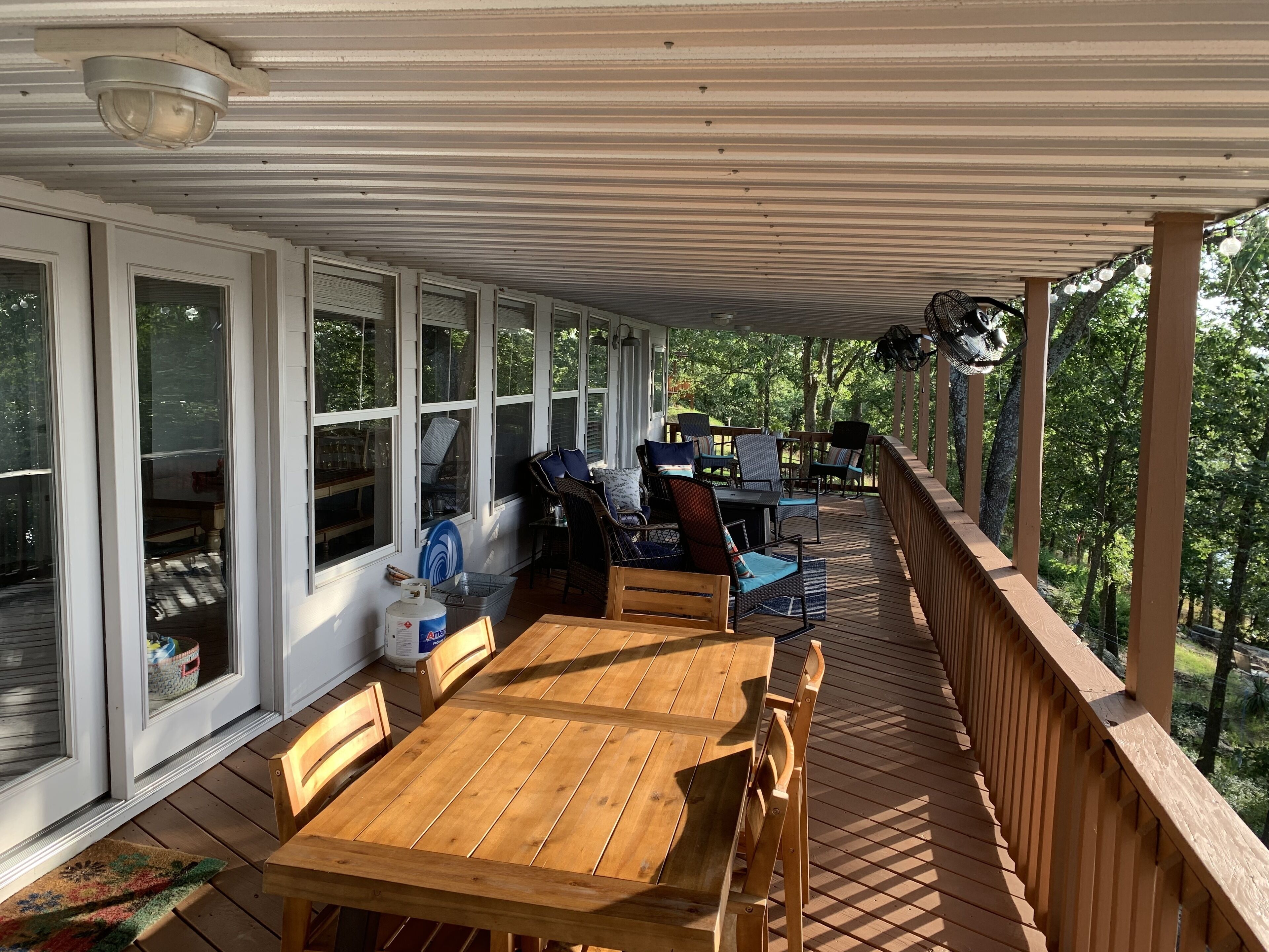 Terraza techada al aire libre con mesa y sillas de madera, rodeada de puertas y ventanas de vidrio, con vistas al exterior.