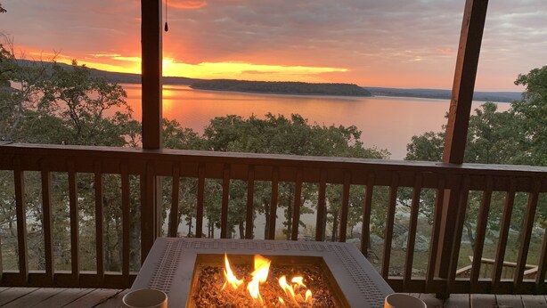A fire pit table with two mugs, overlooking a lake at sunset.