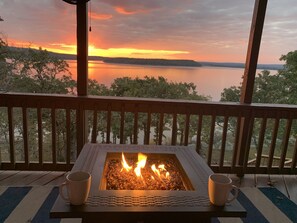 Une table avec foyer intégré, accompagnée de deux mugs, donnant sur un lac au coucher du soleil.