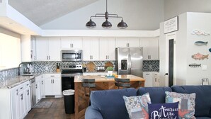 A modern kitchen with white cabinets, a central island, and a blue sofa with decorative pillows.