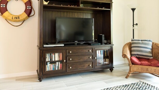 Una sala de estar con un mueble de entretenimiento de madera oscura, un televisor de pantalla plana y un sillón de mimbre con cojines.