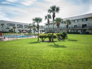 Une cour d’hôtel avec une piscine, des palmiers et une pelouse bien entretenue.