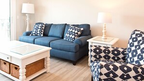 Una sala de estar moderna con un sofá azul, cojines estampados, una mesita de noche blanca y un mueble de almacenamiento de mimbre.