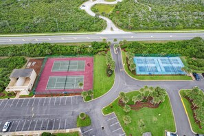 An aerial view of a sports complex with tennis courts, parking areas, and a road.