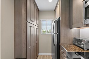 Eine schmale Küche mit Holzschränken, einem Edelstahlkühlschrank, einer Mikrowelle und einem eingebauten Backofen.