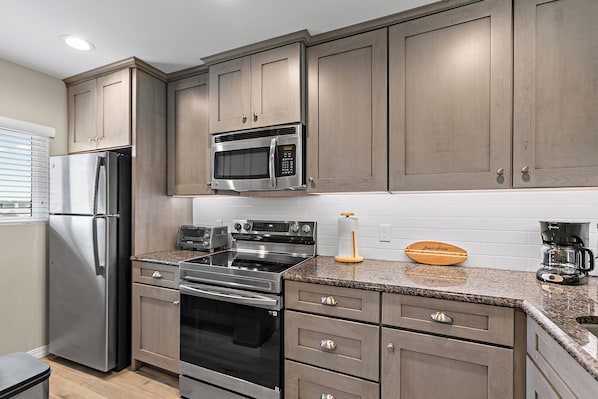 A modern kitchen with stainless steel appliances, wooden cabinets, and a granite countertop.