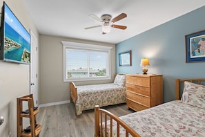 A bedroom with two single beds, a wooden dresser, a ceiling fan, and a window with blinds.