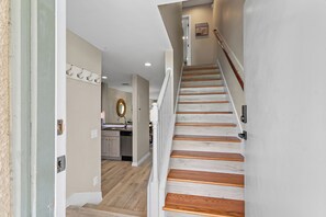 A staircase with wooden steps and a handrail, leading to a landing with a door and a wall-mounted light fixture.