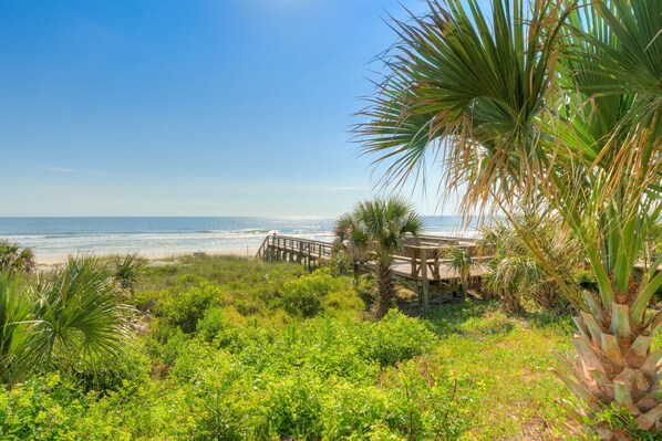 Walk along the boardwalk to the beach, surrounded by lush greenery and ocean views.