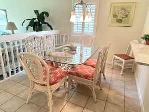 Enjoy meals in this dining area with a glass-top table and wicker chairs, surrounded by a balcony with a potted plant.