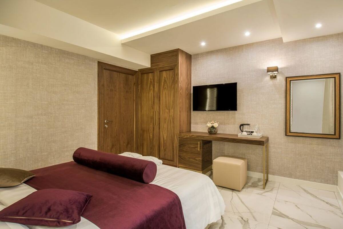 A modern bedroom with a large bed, a wooden wardrobe, a desk with a flat-screen TV, and a mirror on the wall.