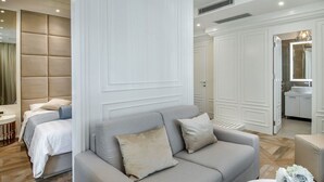 A modern hotel room with a grey sofa, a bed with white linens, and a large mirror in the corner. - Miraval Luxury Rooms (Split)