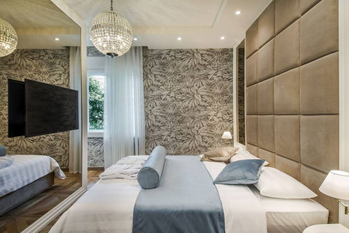 A modern hotel room with a large bed, a TV, and a chandelier.