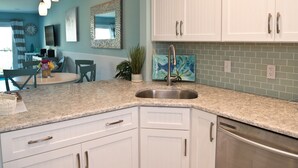 Cucina con mobili bianchi, piano di lavoro in granito, lavello in acciaio inossidabile e backsplash con piastrelle verdi.