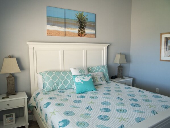 A bedroom with a bed, nightstands, and a wall-mounted painting of a beach scene.