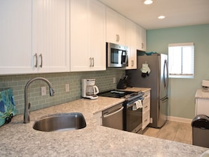 A kitchen with white cabinets, stainless steel appliances, a granite countertop, and a window with blinds.