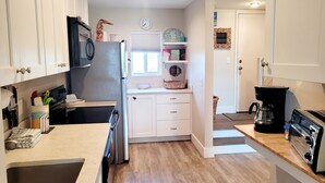 Una cocina moderna con armarios blancos, un refrigerador de acero inoxidable, una cafetera y un tostador.