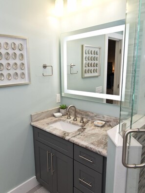 A bathroom with a marble sink, dark cabinets, a glass shower enclosure, and a framed picture of seashells on the wall. - Watch the ocean from your couch! Townhouse at Summerhouse 161 (ST. AUGUSTINE)