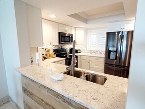 A modern kitchen with white cabinets, stainless steel appliances, and a marble countertop. - Oceanfront 3 bedroom fully furnished at Crescent Beach Summerhouse 166 (ST. AUGUSTINE)